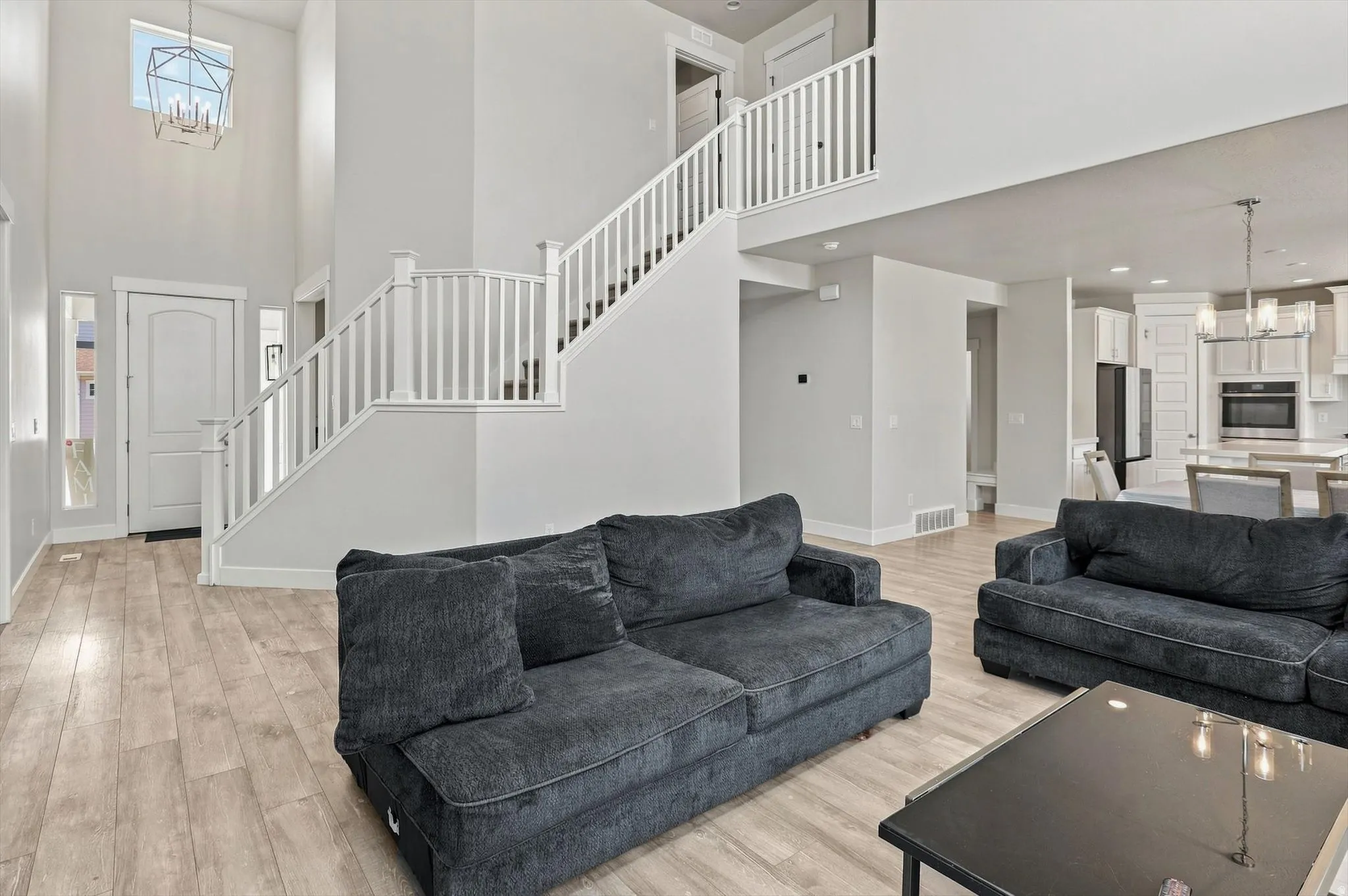 Two-story foyer with a geometric pendant light fixture, wood-finish flooring, white staircase with balusters, and an open-concept kitchen beyond