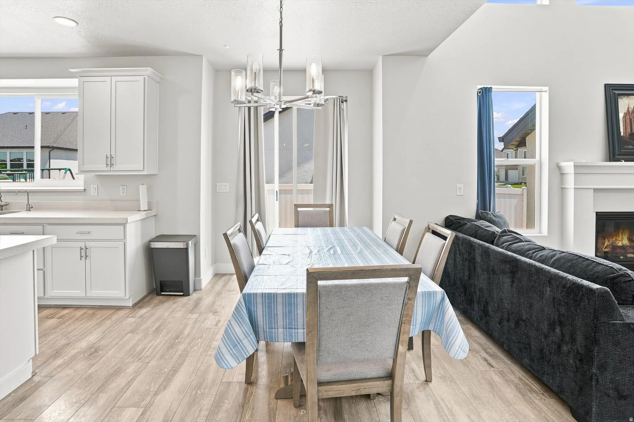 Open-concept living space with wood-finish flooring, white cabinetry, a built-in fireplace, and a dining area featuring a chandelier