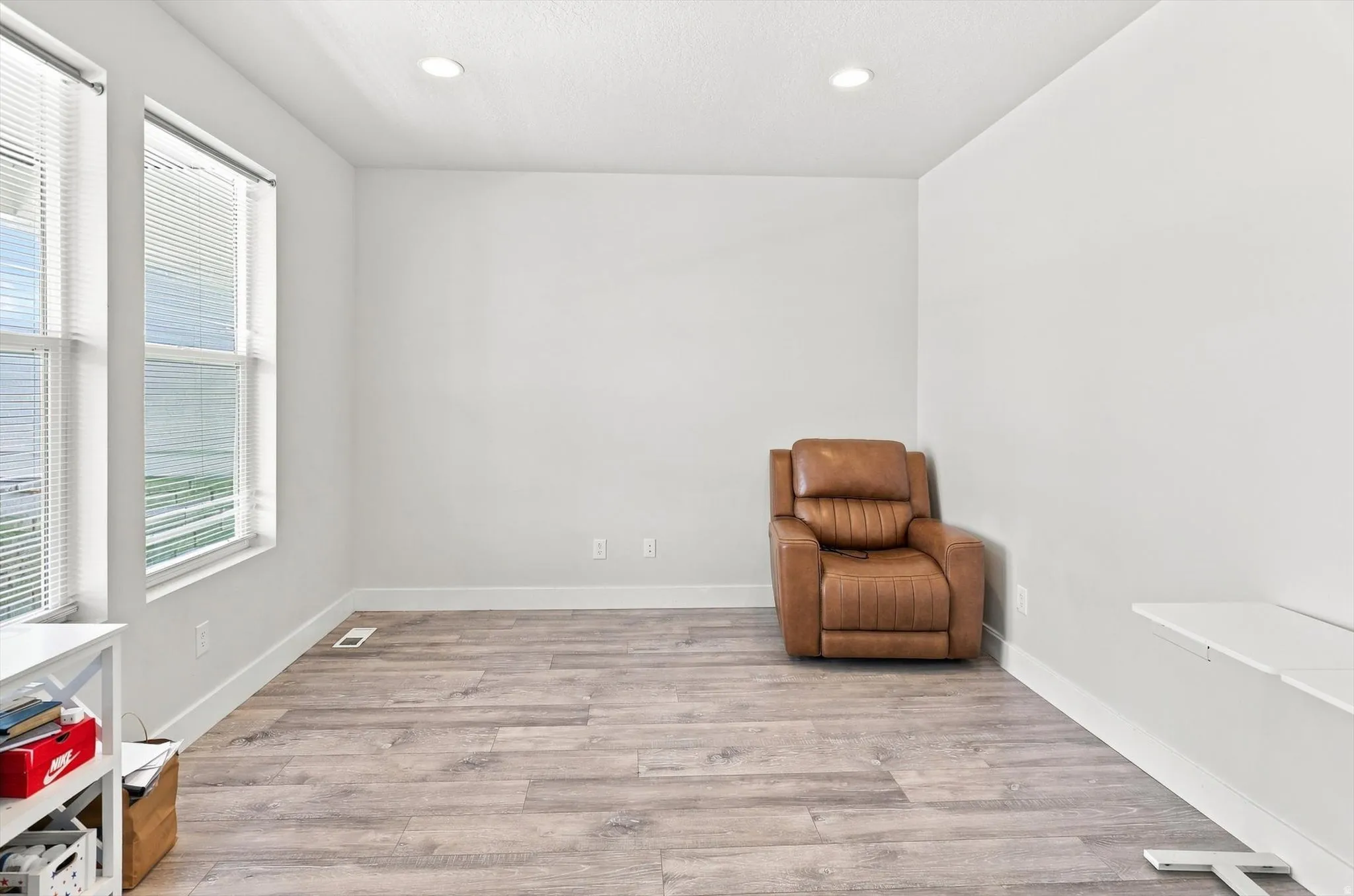Bright, light-filled room featuring dual large windows with blinds, wood-finish plank flooring throughout, and recessed ceiling lighting