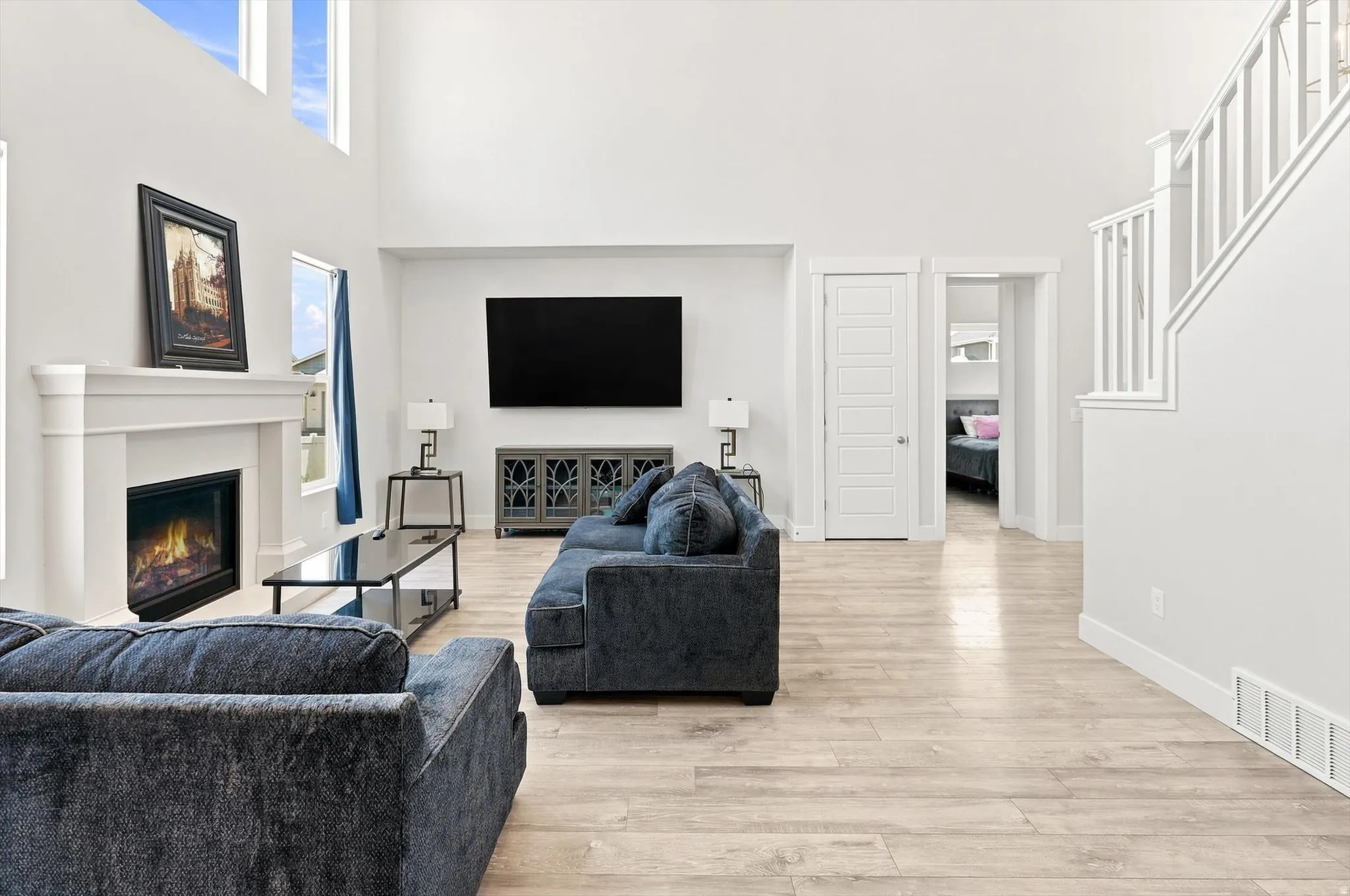 Spacious open-concept living area featuring light wood-finish flooring, a gas fireplace with surround millwork, a wall-mounted flat-screen television, built-in media cabinetry, and abundant natural light from upper windows