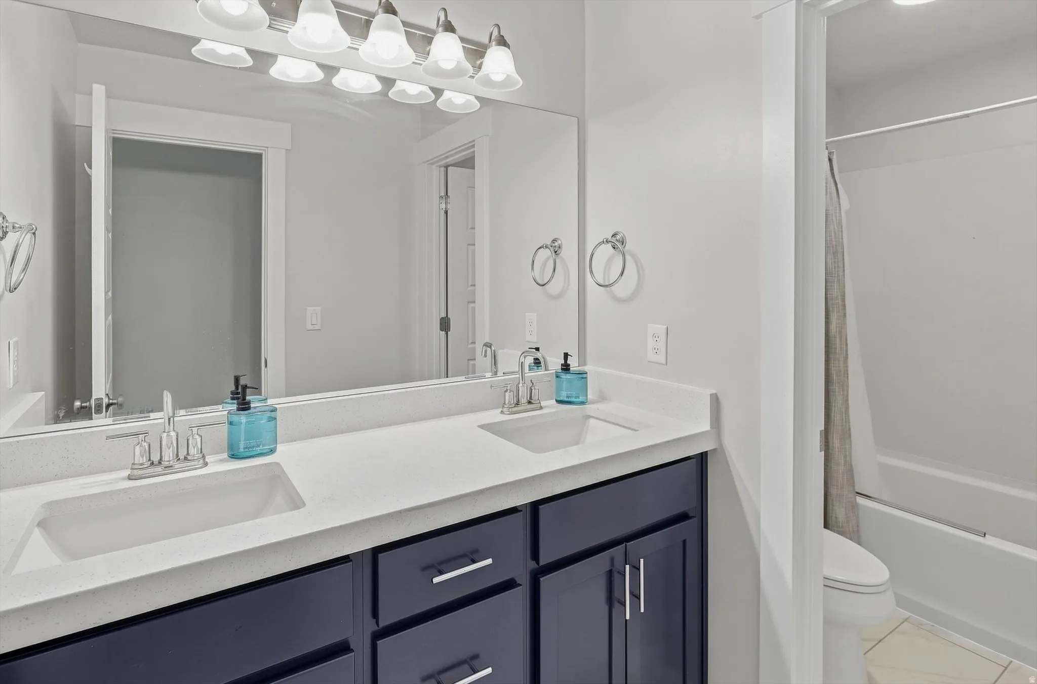 Spa-inspired master bathroom featuring a dual-sink vanity with white quartz countertop, navy cabinetry with chrome hardware, and polished chrome faucets