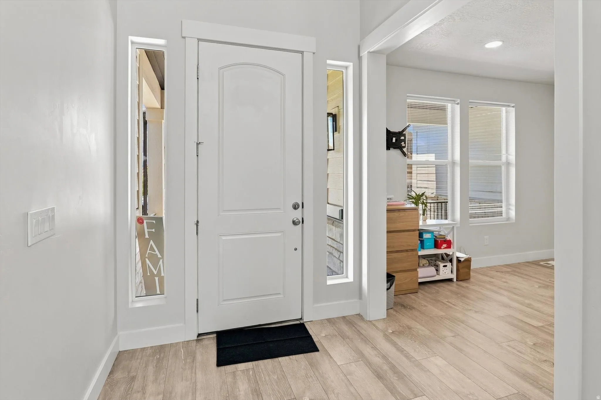 White paneled entry door with sidelight windows, light wood-finish flooring, and white painted walls