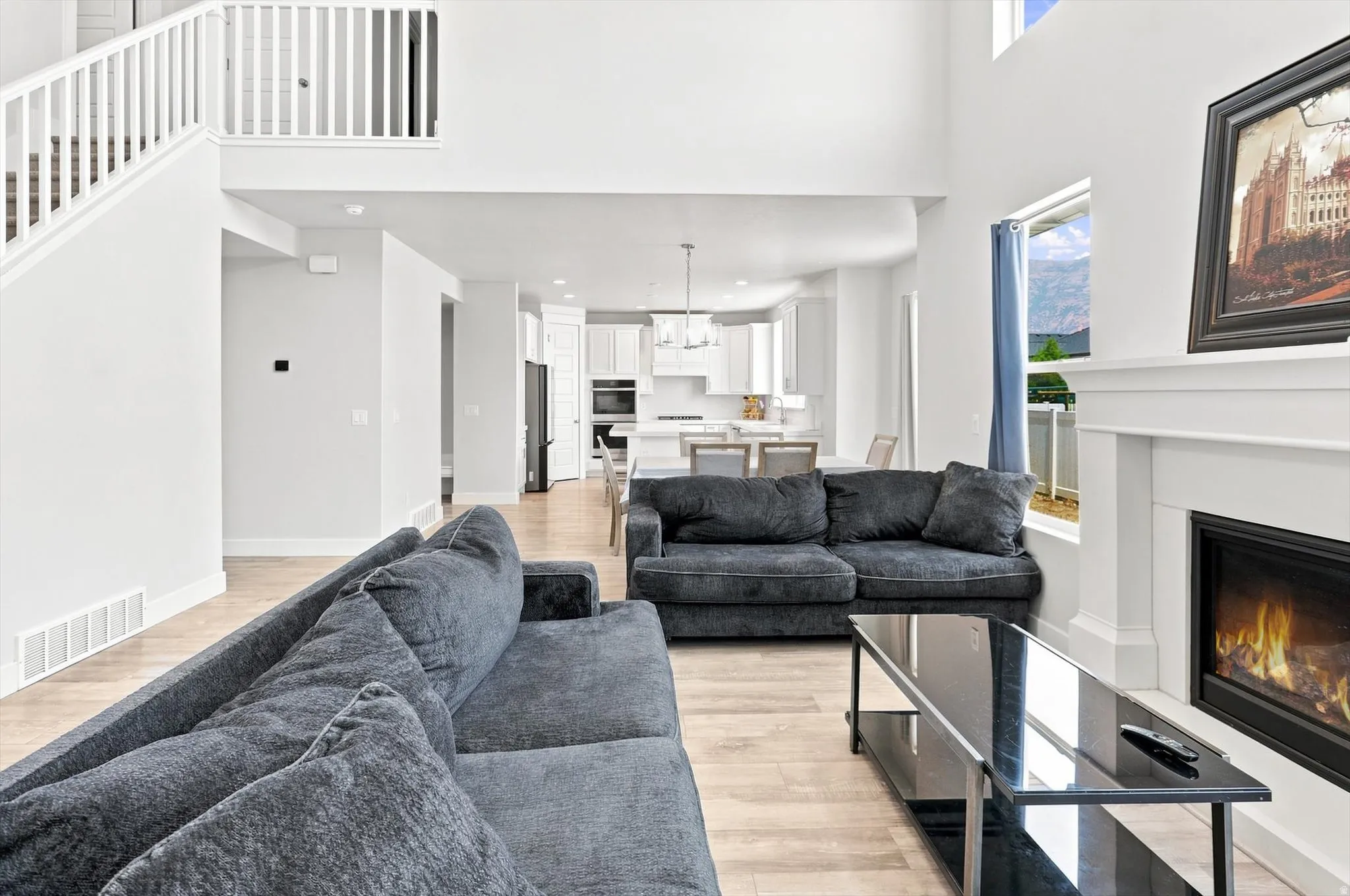 Open-concept living space showcasing a wood-finish plank floor, dual gray upholstered seating areas, and a gas fireplace with a white surround and black metal frame