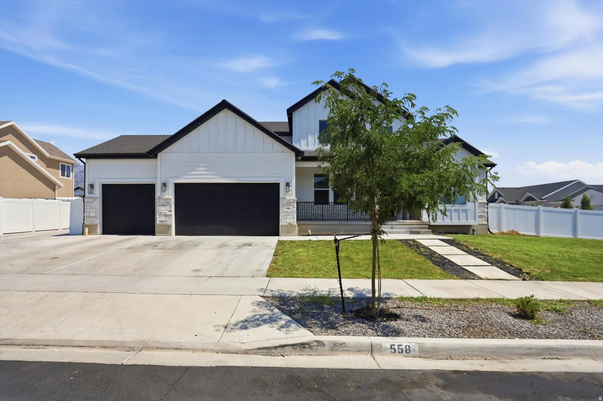 Welcoming two-car garage with black overhead doors, concrete driveway, and mature landscaping anchoring the front elevation