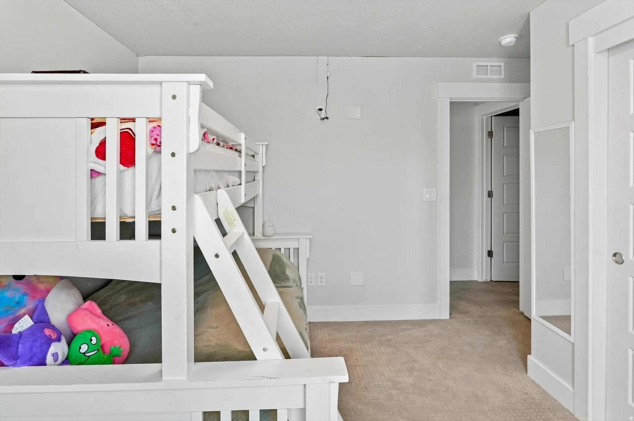 Bright, open bedroom suite featuring a white loft bed with integrated storage and play space beneath, wood-finish flooring throughout, and direct access to an ensuite bathroom