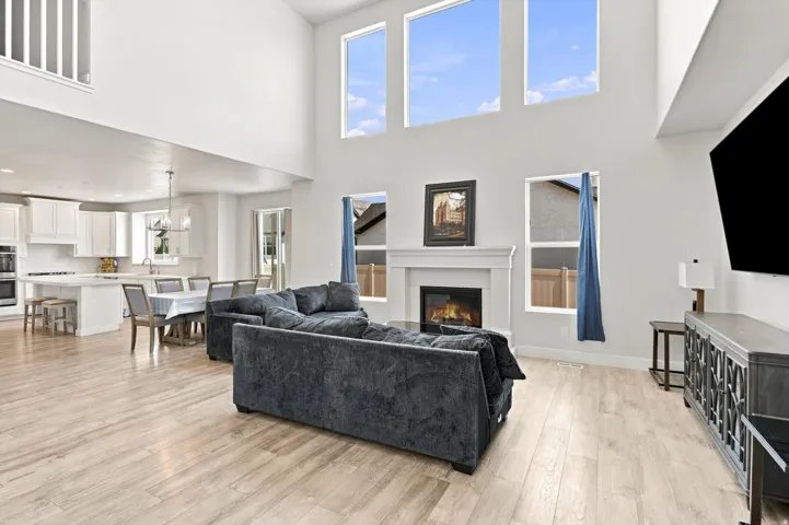 Vaulted living area featuring wood-finish flooring, a white mantel fireplace, and high windows