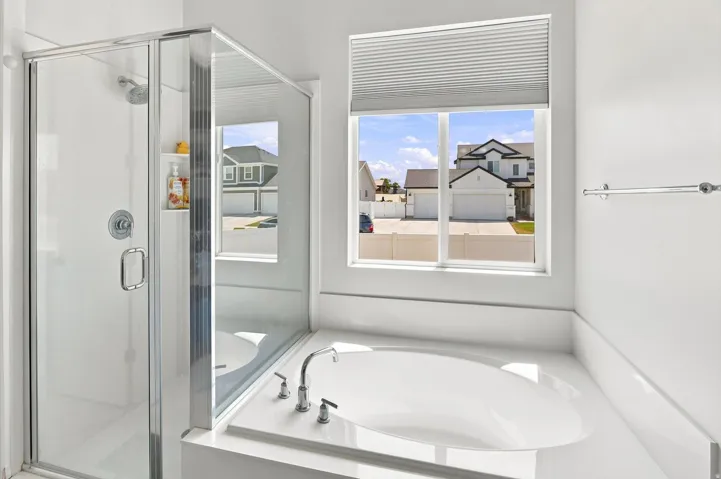 Glass-enclosed shower, built-in shower shelf, soaking tub, window with pleated blind, and polished chrome fixtures
