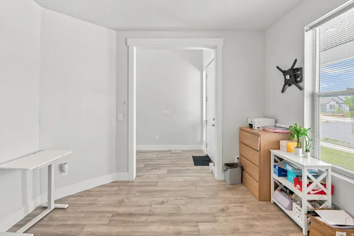 Bright, open room featuring wood-finish flooring throughout, white painted walls, and abundant natural light from large windows with blinds
