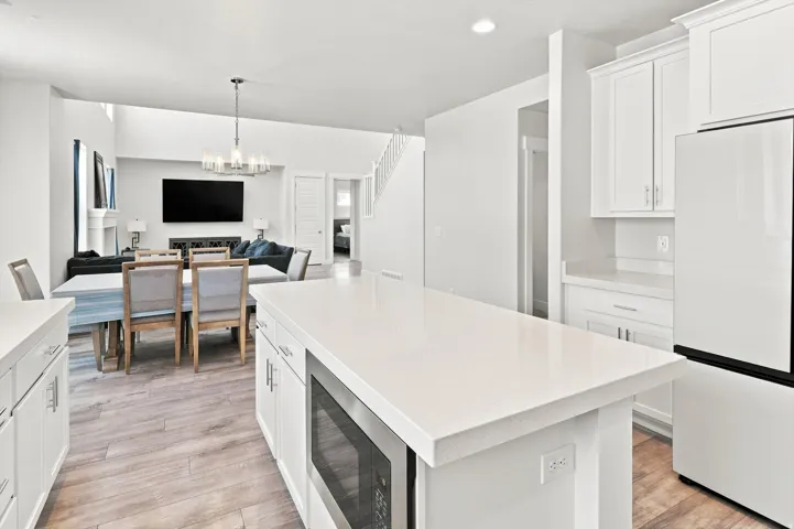 Modern kitchen featuring white cabinetry with integrated hardware, a large waterfall-edge island with white quartz countertop, stainless steel appliances including a built-in microwave, and wood-finish flooring throughout