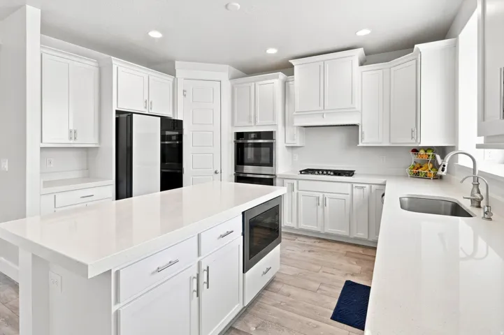 White cabinetry, light-toned wood-finish flooring, built-in double ovens, stainless steel sink, and a large central island