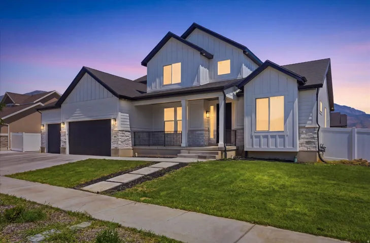 Modern two-story residence featuring a distinctive peaked roofline with multiple gables, board-and-batten siding in gray tones, and stone accents at the foundation