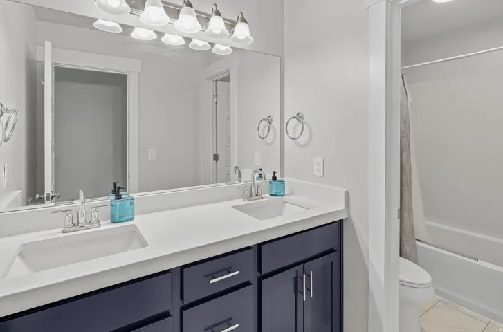 Spa-inspired master bathroom featuring a dual-sink vanity with white quartz countertop, navy cabinetry with chrome hardware, and polished chrome faucets