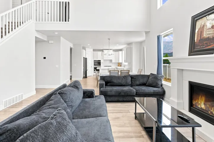 Open-concept living space showcasing a wood-finish plank floor, dual gray upholstered seating areas, and a gas fireplace with a white surround and black metal frame