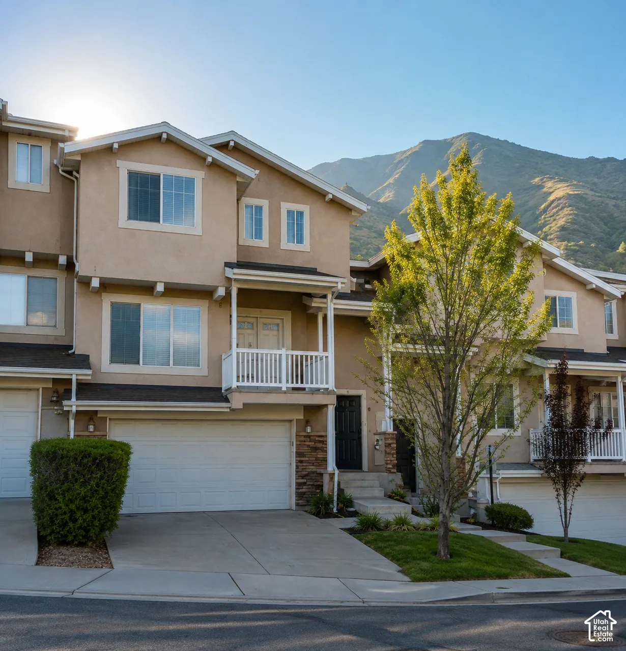 Contemporary townhome with a stucco exterior, integrated garage, upper-level balcony, and a mountain backdrop