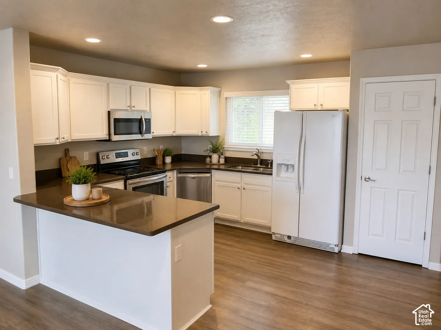 Bright, open-concept kitchen featuring cream cabinetry, stainless steel appliances including a built-in microwave and range, dark wood-finish countertops, a large center island with seating space, and wood-finish flooring throughout