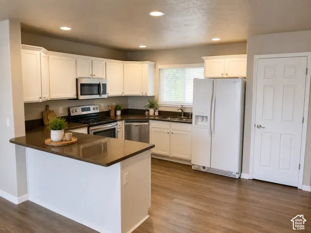 Bright, open-concept kitchen featuring cream cabinetry, stainless steel appliances including a built-in microwave and range, dark wood-finish countertops, a large center island with seating space, and wood-finish flooring throughout