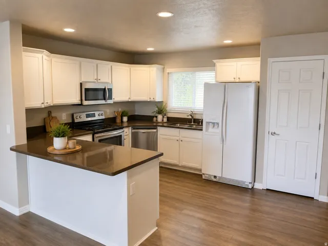 Bright, open-concept kitchen featuring cream cabinetry, stainless steel appliances including a built-in microwave and range, dark wood-finish countertops, a large center island with seating space, and wood-finish flooring throughout