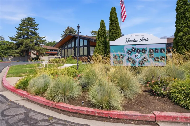 Property entry featuring a community map display, evergreen trees, a flagpole with an American flag, and a modern building with expansive windows