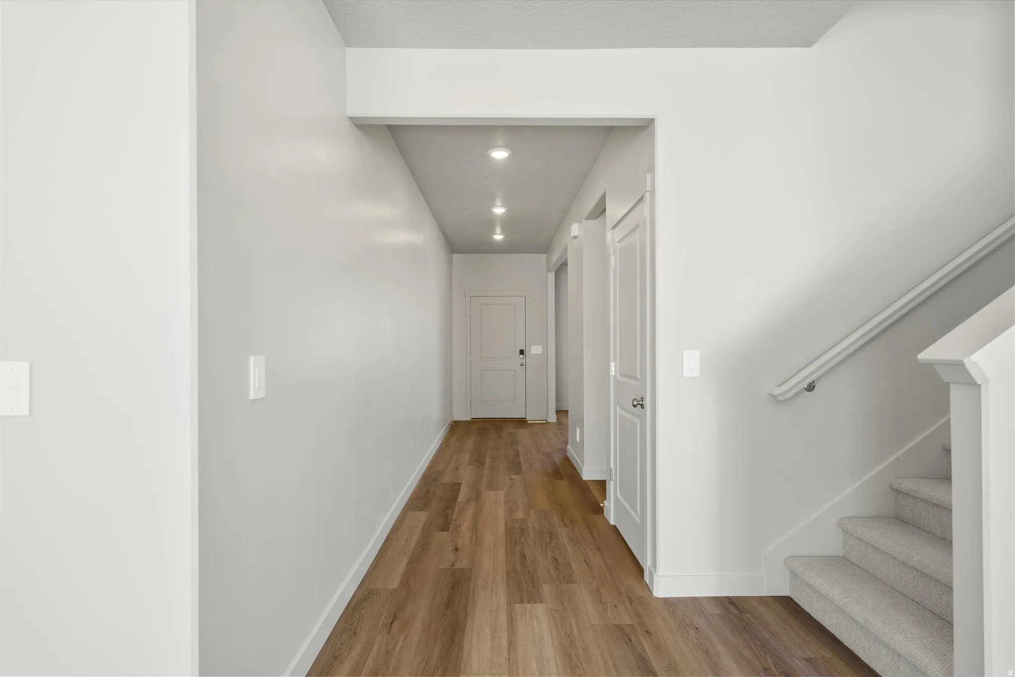**DISCLAIMER** Interior package may vary. Hallway featuring wood-finish flooring, recessed lighting, white panel doors, and a carpeted staircase with a white handrail
