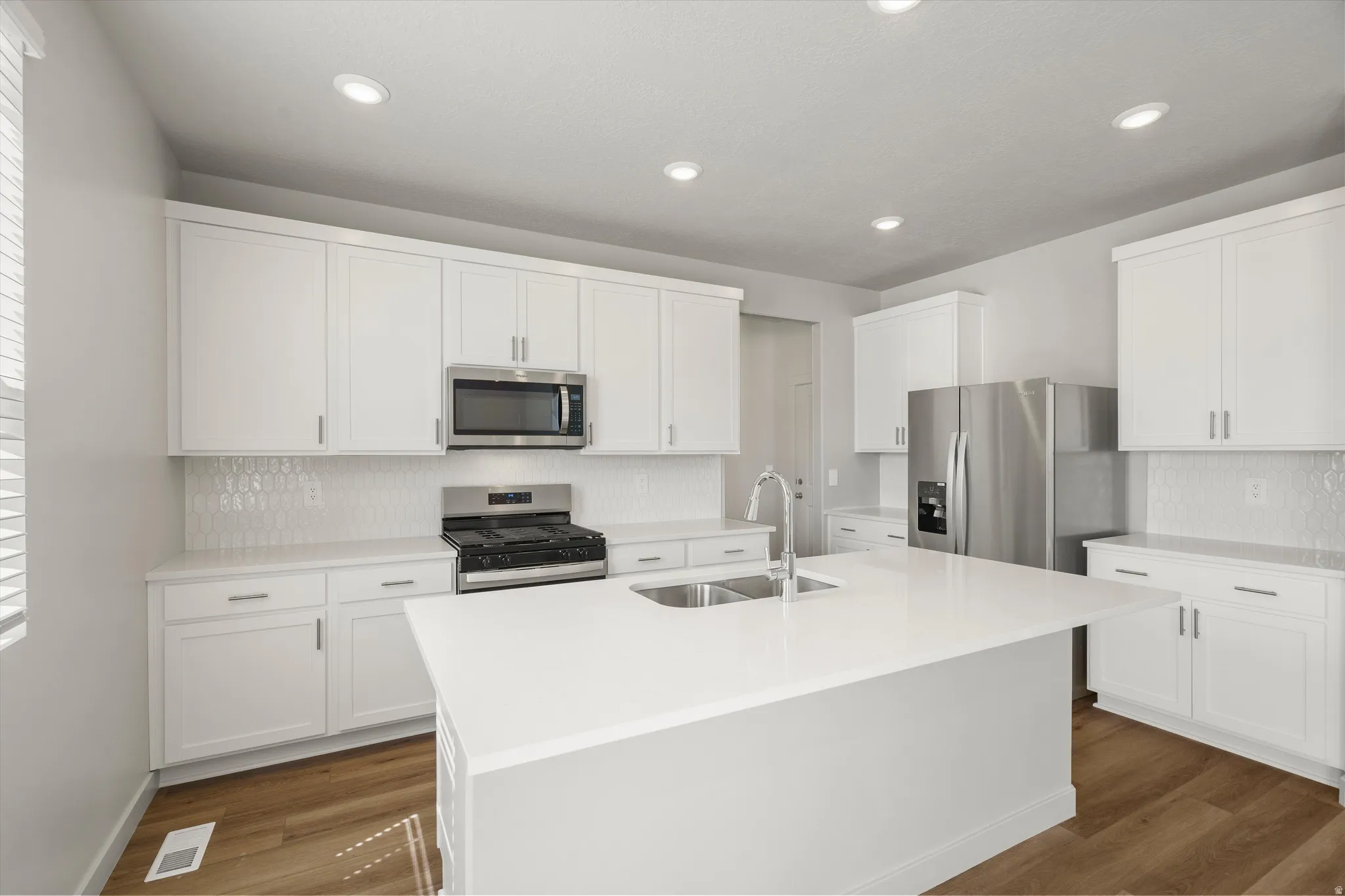 **DISCLAIMER** Interior package may vary. Modern kitchen featuring white cabinetry with stainless steel hardware, quartz countertops, a large waterfall-edge island, stainless steel appliances including a gas range and over-the-range microwave, subway tile