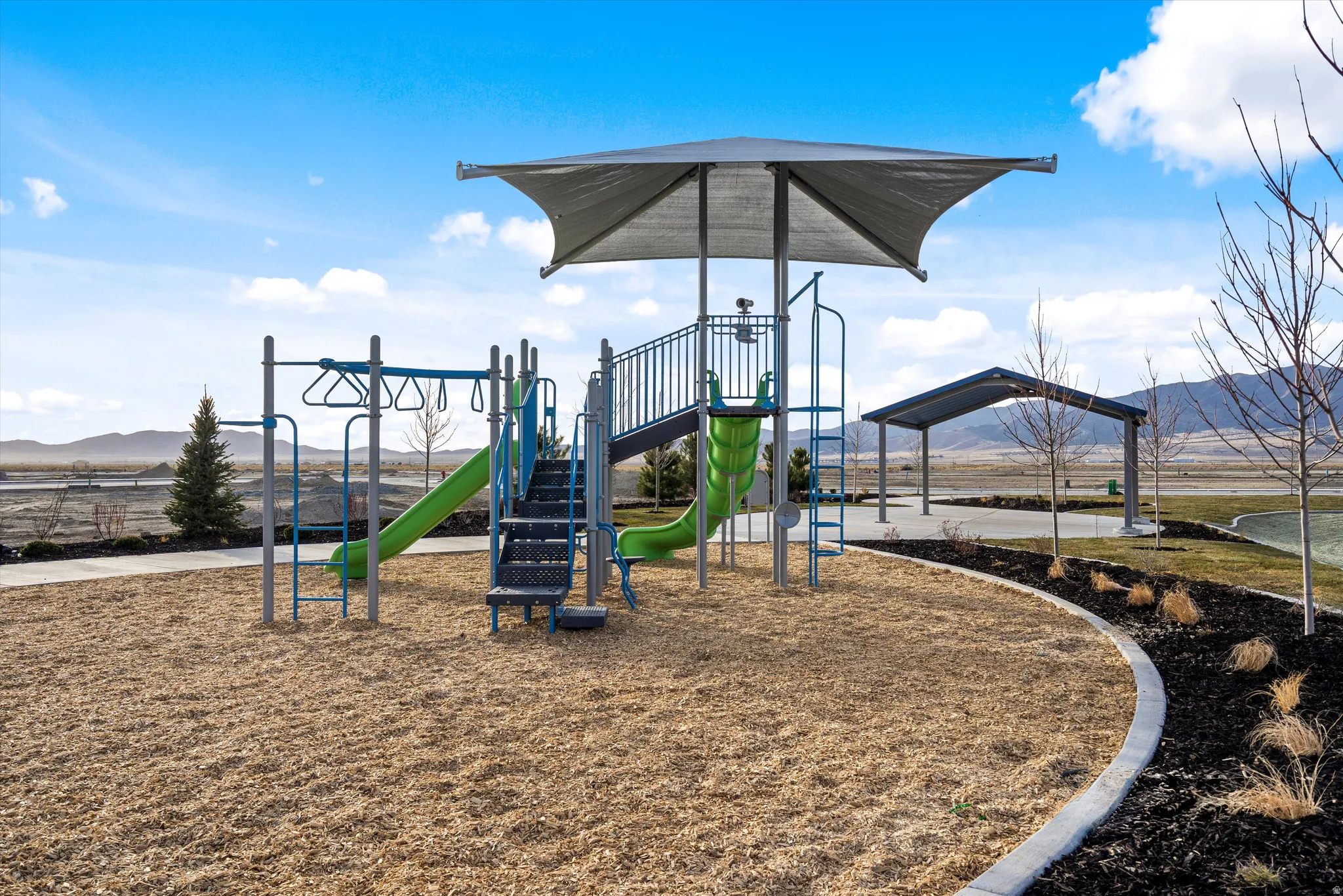 Playground area featuring a shade structure, multiple slides, monkey bars, and a paved path