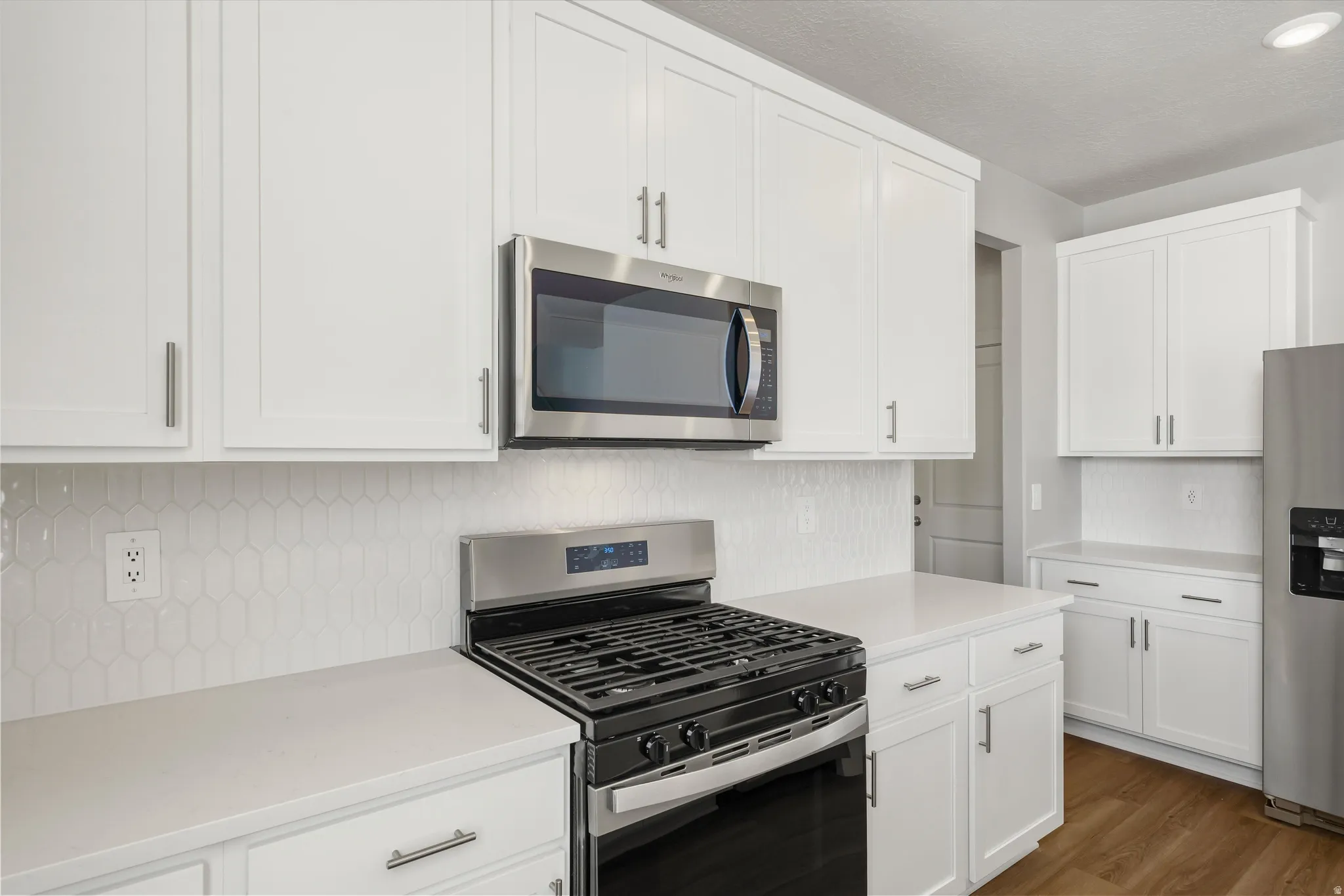 **DISCLAIMER** Interior package may vary. White shaker cabinetry with brushed nickel hardware, light-toned countertops, geometric pattern tile backsplash, and stainless steel appliances