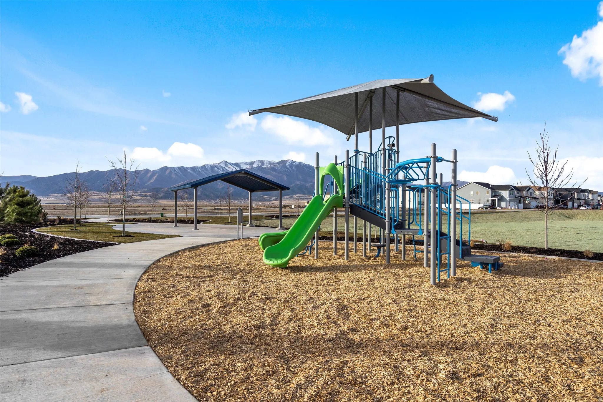 Community playground featuring a multi-level play structure with a slide, protective shade canopy, and wood chip surfacing
