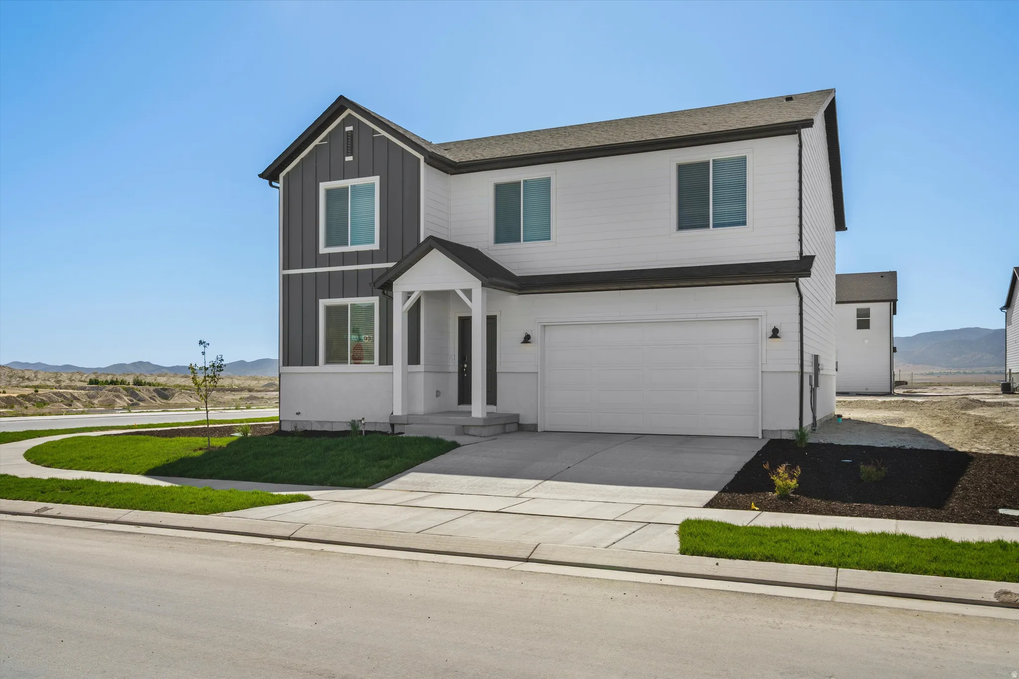 Modern two-story residence featuring a striking two-tone exterior with charcoal and cream siding, complemented by a peaked gable entry