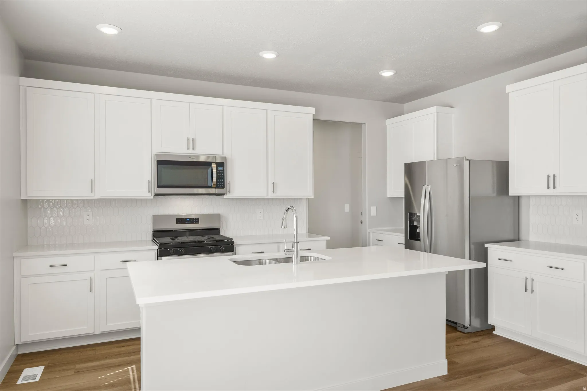 **DISCLAIMER** Interior package may vary. Kitchen featuring white cabinetry, stainless steel appliances, a center island with sink, white countertops, and wood-finish flooring