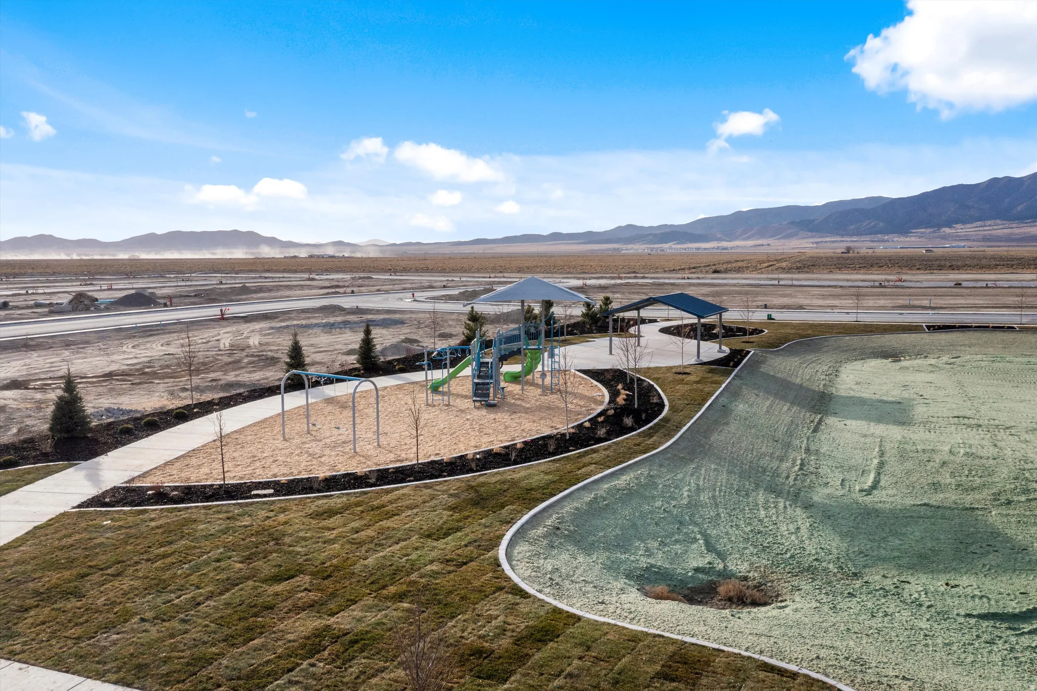 Modern recreational amenities set within expansive grounds featuring a custom playground structure with multiple play components, curved walking pathways with metal railings, manicured lawn areas, and mountain vistas across the property