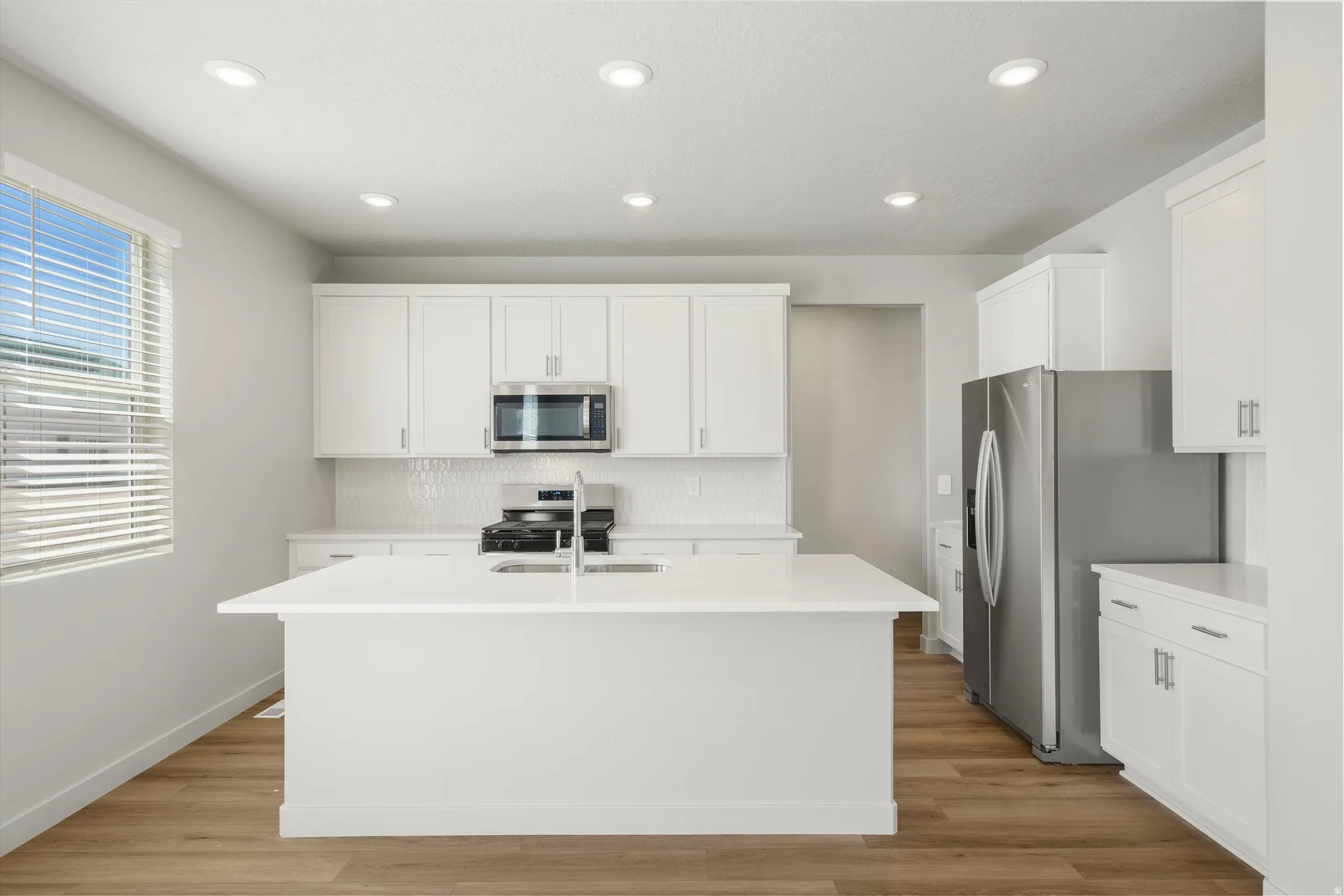 **DISCLAIMER** Interior package may vary. White cabinetry, stainless steel appliances, central island with sink, wood-finish flooring, and recessed lighting