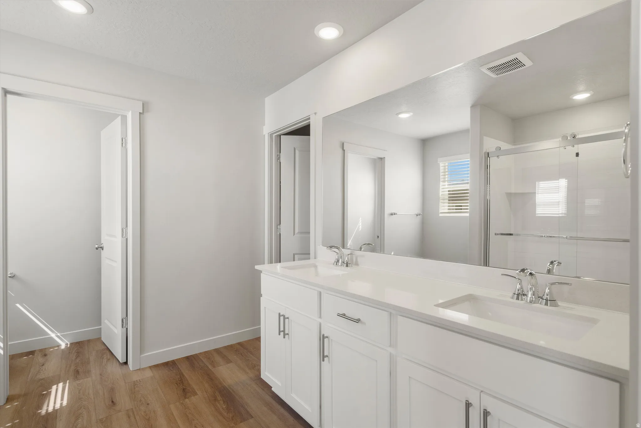 **DISCLAIMER** Interior package may vary. Dual vanity with integrated sinks, wood-finish flooring, recessed lighting, and a glass-enclosed shower
