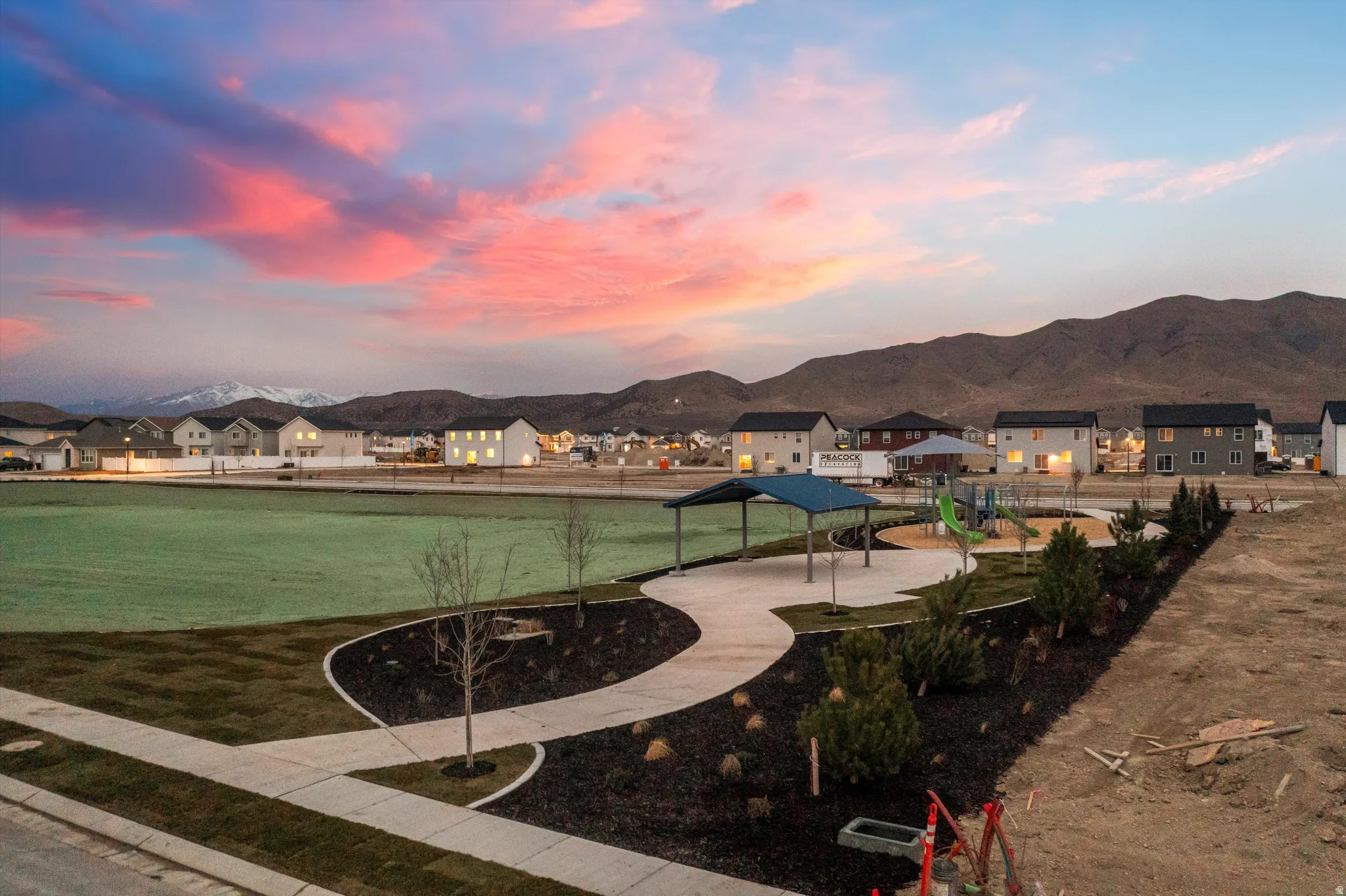 Expansive green space featuring a playground, covered recreation area, and paved walking paths, all set against a backdrop of distant mountains