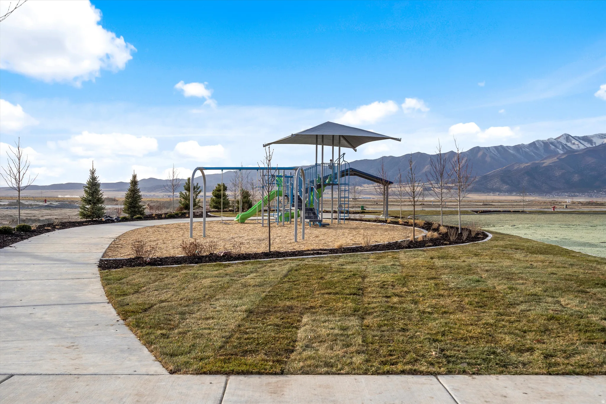 Community playground with a swing set and slide, featuring a covered play structure