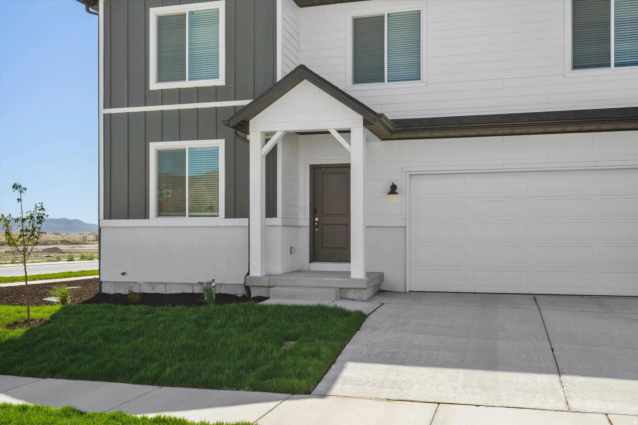 Two-tone exterior siding, covered entryway, prominent garage door, concrete driveway, and manicured landscaping