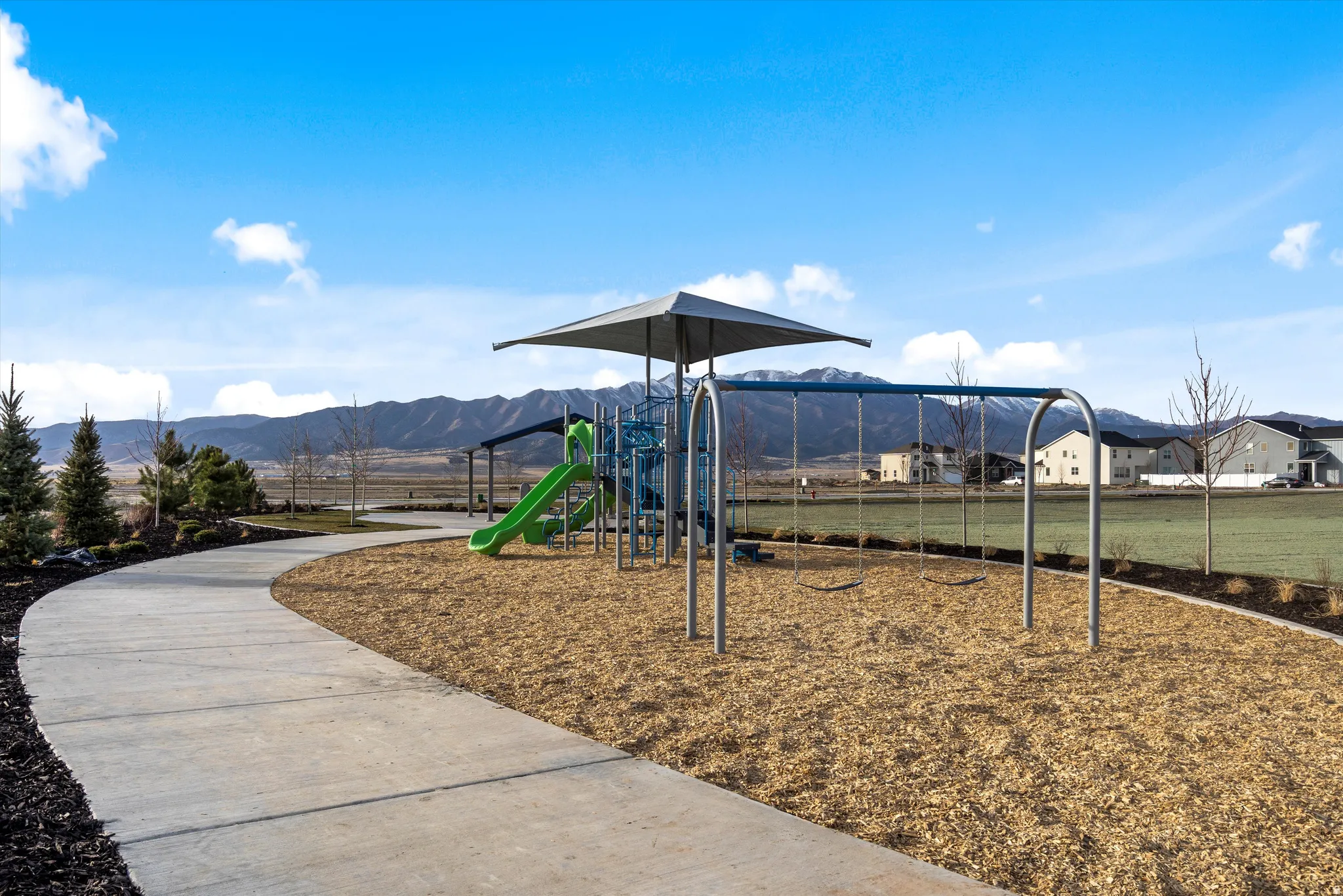 Community playground with swings and a slide, featuring a shade structure and a paved walking path