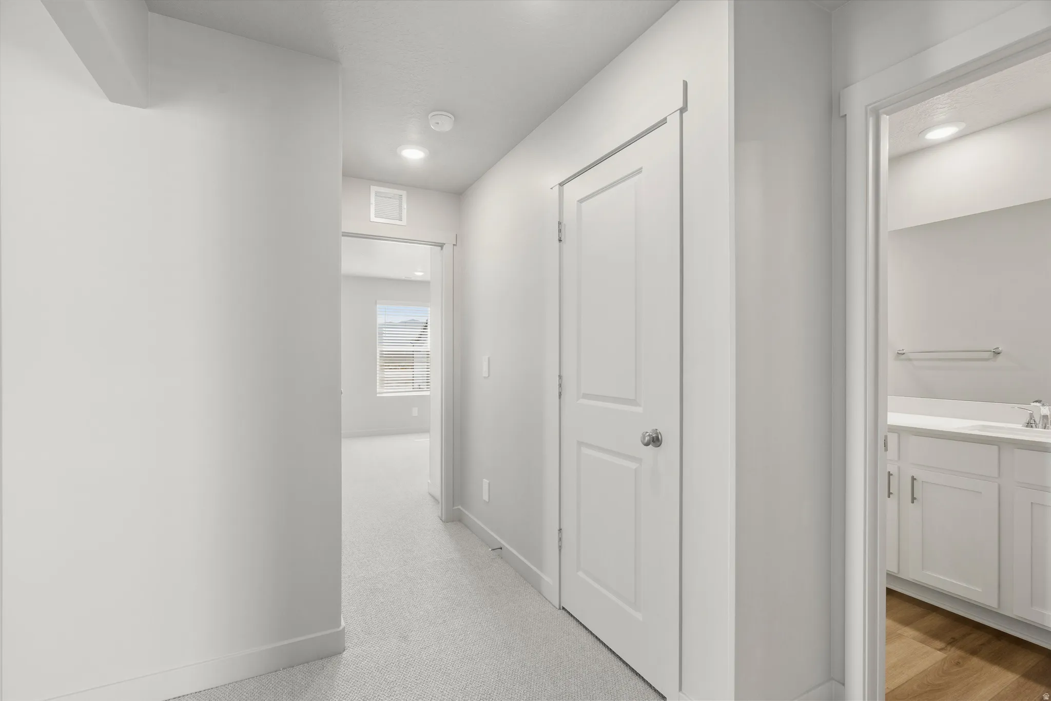 **DISCLAIMER** Interior package may vary. Hallway with recessed lighting, carpet flooring, paneled interior doors, and a bathroom featuring a white vanity with an integrated sink and wood-finish flooring
