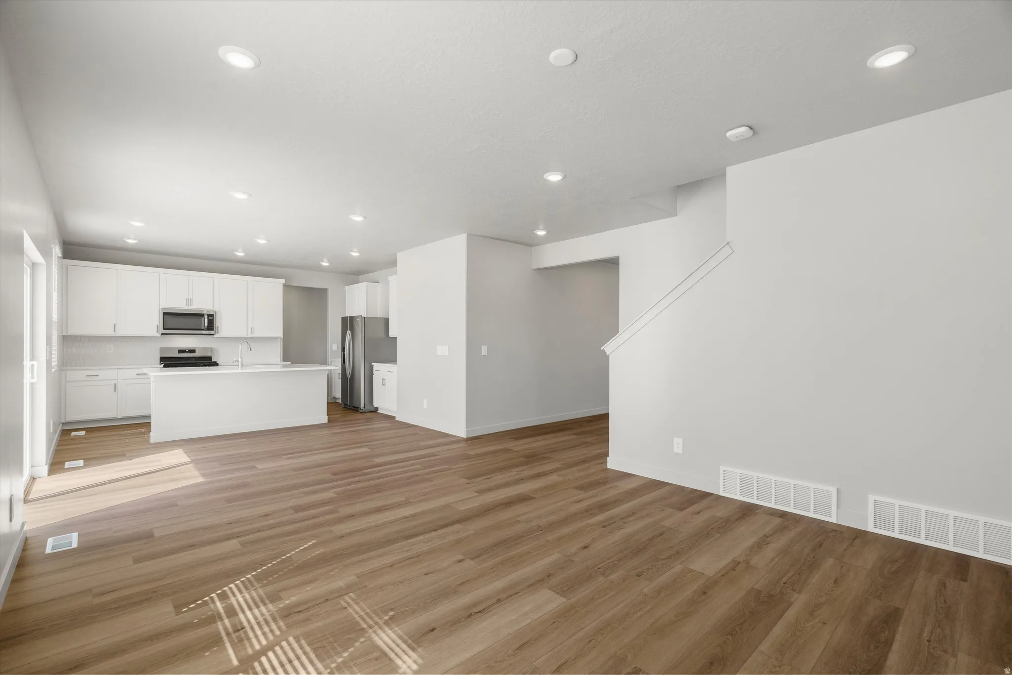 **DISCLAIMER** Interior package may vary. Open-concept living area with warm wood-finish flooring throughout, recessed lighting, and seamless integration with a modern kitchen featuring white cabinetry, stainless steel appliances, and quartz countertops