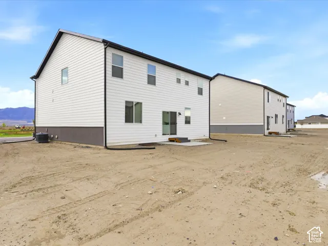 Two-story exterior featuring white horizontal siding, dark-toned masonry foundation, black gutter system, sliding glass door, and rear concrete patio