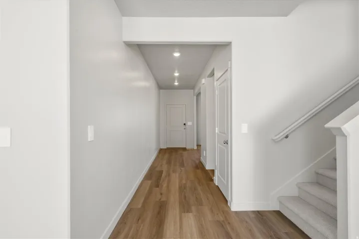 **DISCLAIMER** Interior package may vary. Hallway featuring wood-finish flooring, recessed lighting, white panel doors, and a carpeted staircase with a white handrail