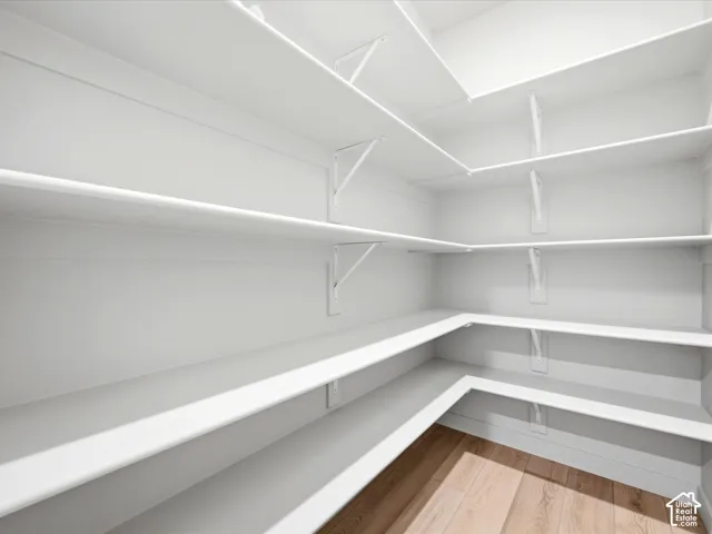 Walk-in storage space featuring multi-level wrap-around shelving supported by metal brackets and wood-finish flooring