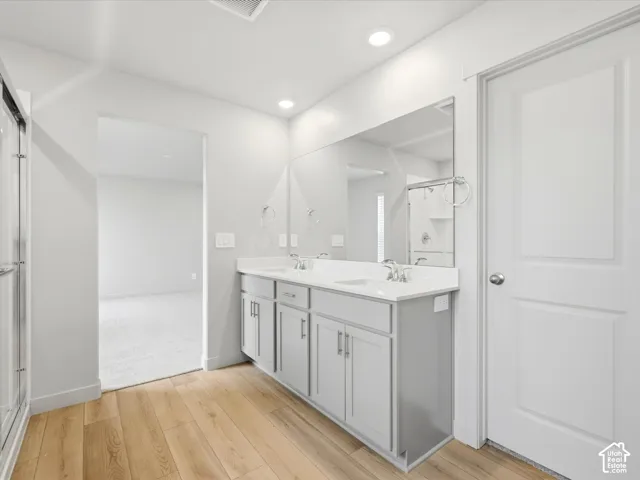 Bathroom featuring a dual-sink vanity with light-colored cabinetry, a neutral solid-surface countertop, recessed ceiling lighting, and wood-finish flooring