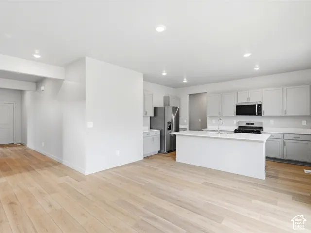 Kitchen featuring light-toned cabinetry, an island with a stone-finish countertop, stainless steel appliances, and wood-finish flooring throughout