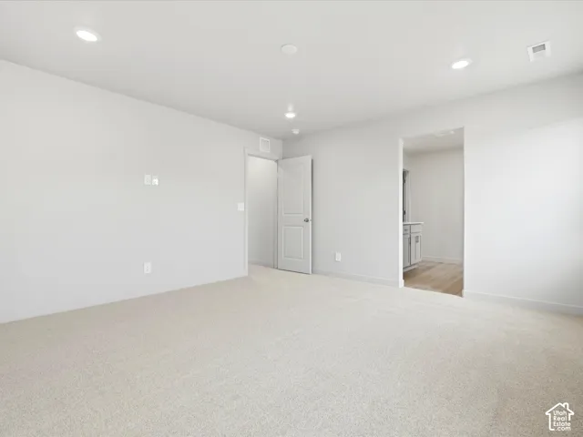 Interior room featuring neutral wall-to-wall carpeting, recessed ceiling lighting, and a solid-core interior door with satin nickel hardware