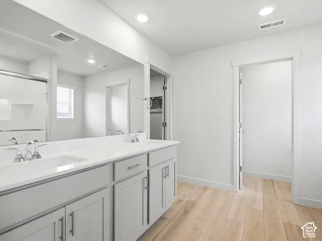 Dual-sink vanity with light gray shaker-style cabinetry, solid-surface countertop, recessed lighting, and wood-finish flooring