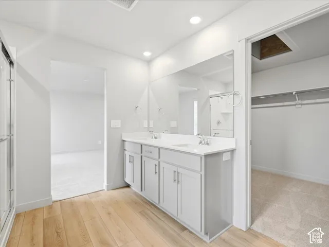 Dual-sink vanity with light-tone cabinetry and stone-surface countertop, full-width vanity mirror, recessed ceiling lighting, glass-enclosed shower, and wood-finish flooring