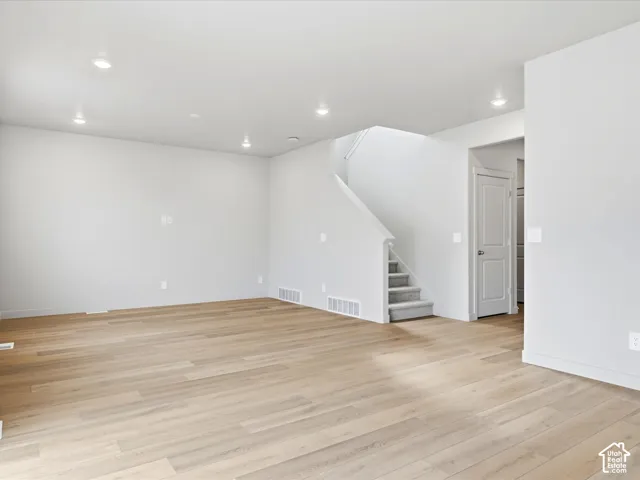 Open-concept room with wood-finish flooring, recessed lighting, and a staircase featuring carpeted steps and a white railing
