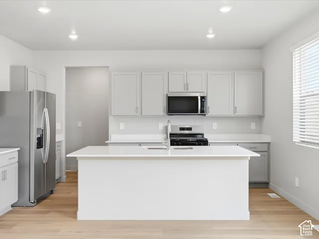Kitchen featuring a central island with a solid-surface countertop, shaker-style cabinetry, stainless steel appliances, and wood-finish flooring