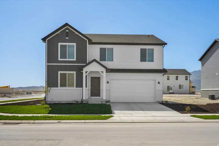 Two-story residence featuring a dark gray and white exterior, an attached two-car garage, a covered entry porch, a paved driveway, and manicured landscaping