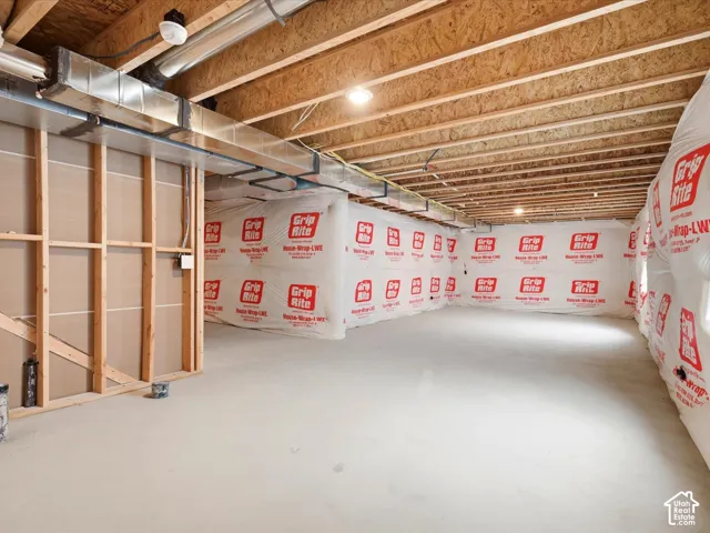 Unfinished lower level featuring exposed wood framing, concrete flooring, house-wrap interior wall protection, and exposed mechanical ductwork